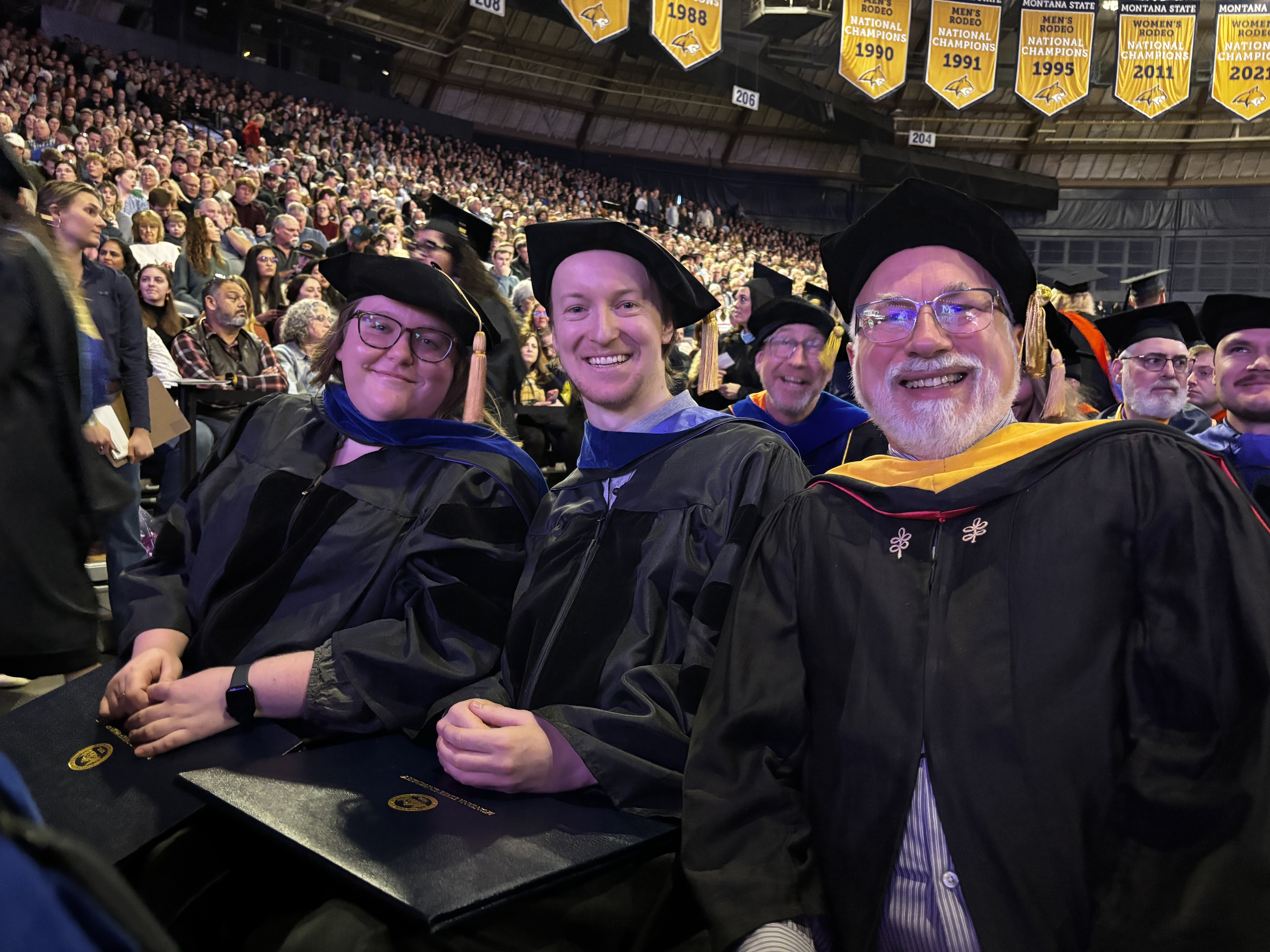 Two students and a professor at a PhD graduation