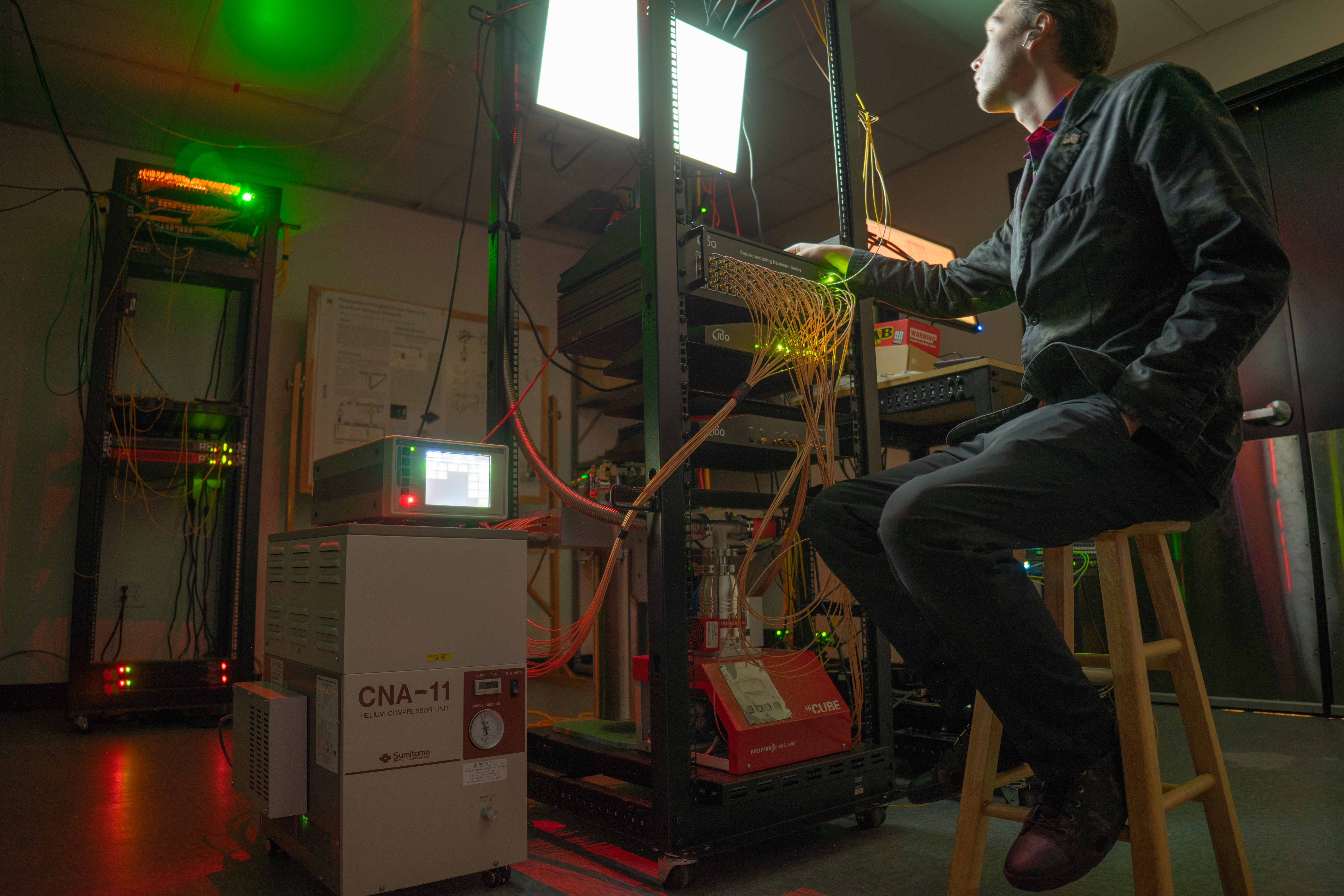 Nathan Kuehl sits at server rack filled with optical fibers